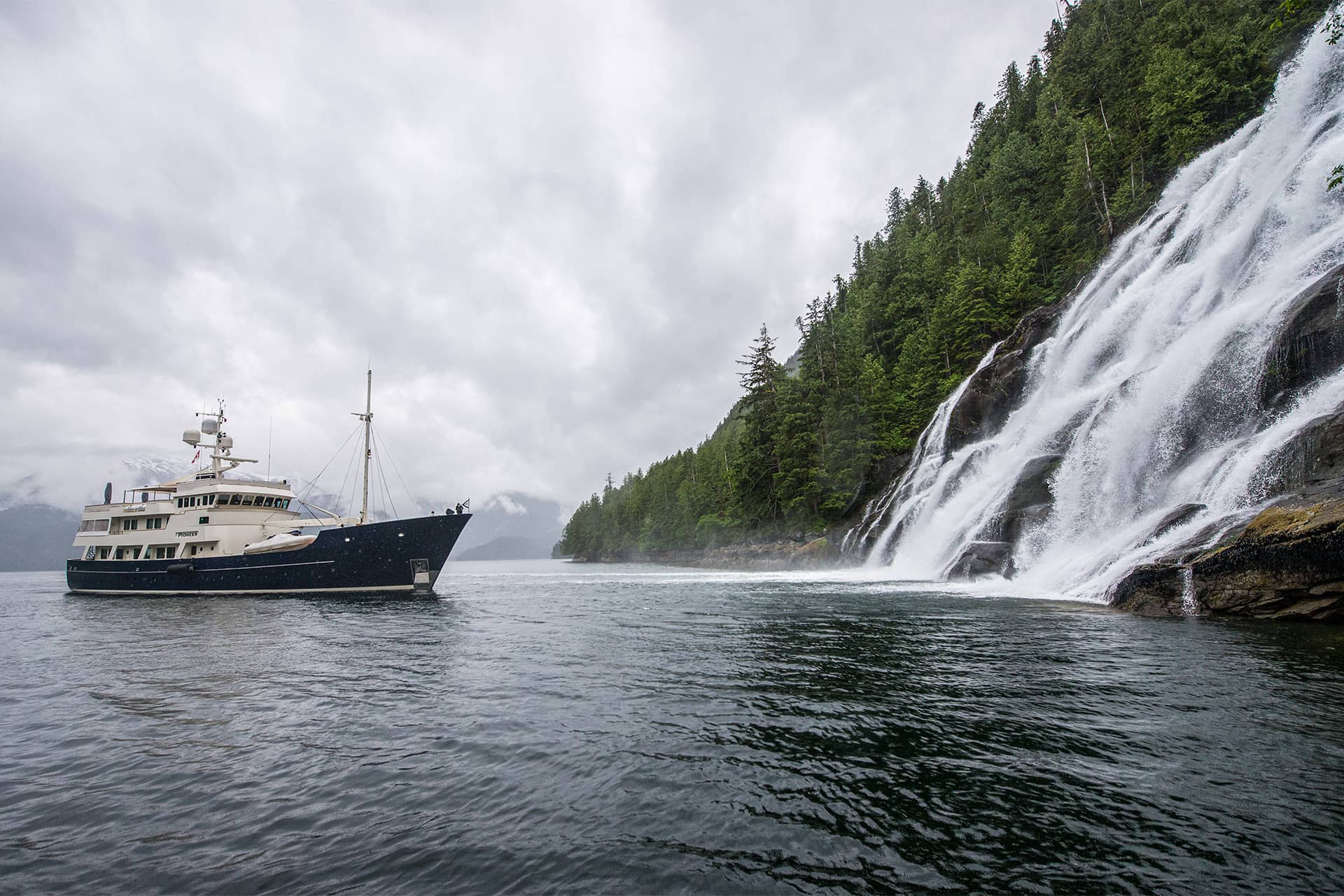 Private yacht beside a dramatic waterfall on a forested coastline